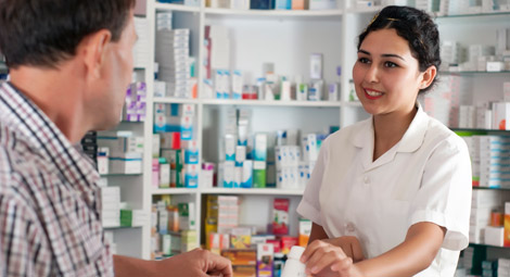 A male pharmacist stood with his arms crossed smiling in front of a shelf of medication